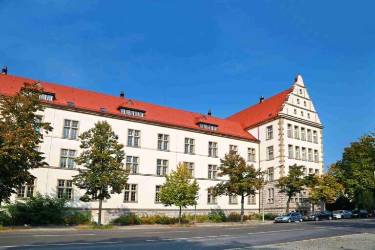 Weißes Gebäude mit rotem Dach vor blauem Himmel aņ Straße mit Bäumen